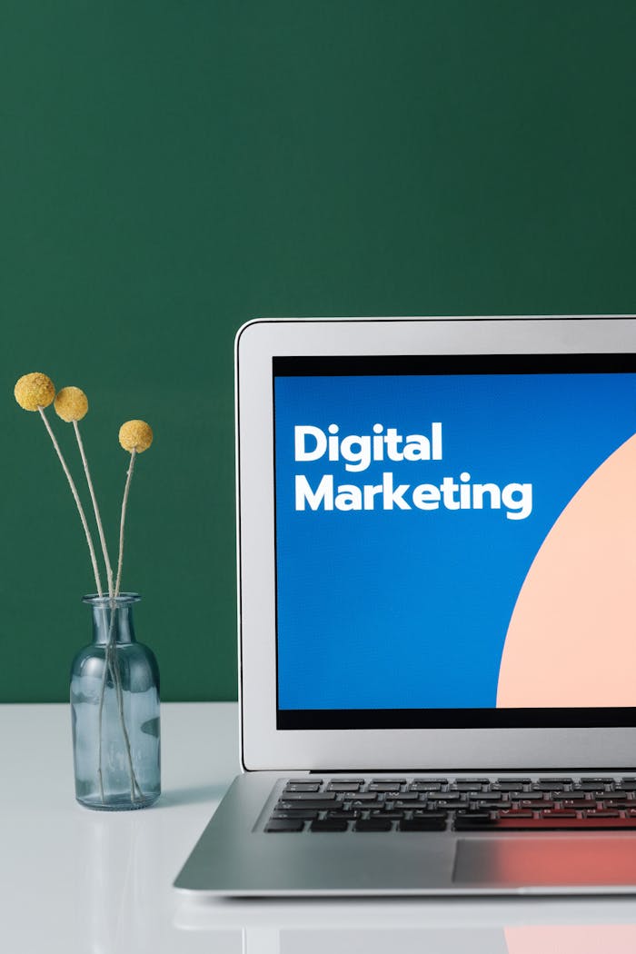 about-us A laptop displaying 'Digital Marketing' with a minimalist floral decor in a glass vase.