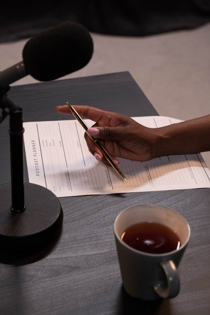 services-02 Close-up of hand holding pen near microphone with tea and planner.